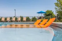 Luxurious outdoor pool area featuring vibrant orange sun loungers, surrounded by lush greenery and shaded seating under a bright blue umbrella.