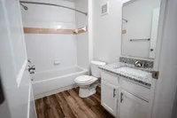 Enjoy the clean, bright feel of this bathroom at The Bristol — featuring a granite countertop sink, hardwood-style flooring, and a shower/tub with crisp white cabinetry and fixtures.