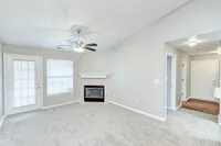 This bright, carpeted living room includes a ceiling fan, cozy fireplace, and access to your own private patio or balcony—plus a welcoming wood-style entryway near the front door.