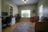 Bright and inviting home office with dual workstations, cozy seating, and a large window offering natural light.