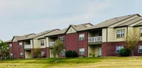 Charming apartment complex with red brick facade, featuring spacious balconies and surrounded by lush greenery and well-maintained lawns.