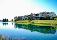 Luxury apartments overlooking a serene pond with lush green surroundings and pristine architecture.