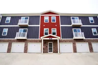 Private garages on the ground floor — just one example how The Ventry is built for daily ease and a little fresh air. Chic three-story apartment building featuring modern balconies and a stylish red and gray facade.