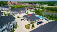 Everything you need, all in one place—from the pool and clubhouse to easy access to local spots. Vibrant aerial view of a modern apartment complex with a swimming pool, surrounded by lush greenery and ample parking space.