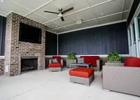 End your day fireside. Our outdoor lounge is made for laid-back evenings and weekend hangouts. Chic outdoor lounge with brick fireplace, cozy red seating, and modern ceiling fan, ideal for relaxation.