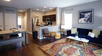 Room to live, cook, and connect—this open-concept layout blends comfort and function in one smart design. Chic open-concept living and dining area featuring a modern kitchen with stainless steel appliances, vibrant artwork, and cozy seating on a colorful patterned rug.