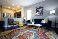From coffee to dinner parties, this seamless layout brings it all together. Chic living area with modern kitchen, cozy seating, vibrant rug, and stylish artwork creating a welcoming ambiance.