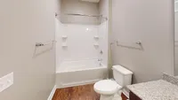 Room to refresh. Clean design meets everyday comfort with a spacious bathroom and convenient shower-tub combo. Modern bathroom featuring elegant granite countertop, sleek white bathtub, and rich hardwood floor.