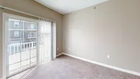 Soft carpet underfoot, fresh air just outside. This bedroom’s private balcony brings in light, breeze, and a quiet escape. Bright and inviting room with plush carpet, large window, and modern white blinds, offering a view of neighboring balconies.