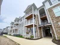 Three-story buildings with arched stairwells and private outdoor space create a clean, modern backdrop for everyday living. Modern apartment complex with elegant balconies and stone accents, offering a contemporary living experience in a suburban setting.