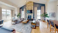 A cozy spot for catching up, kicking back, or letting the fireplace do its thing while the TV plays in the background. Inviting modern living room with vaulted ceiling, sleek stone fireplace, and elegant chandelier, featuring comfortable sofas and abundant natural light.