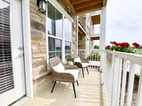 Your own balcony with room to relax, read, or catch some fresh air in peace. Charming apartment patio with cozy wicker chairs, vibrant red flowers, and elegant stone siding, offering a serene outdoor retreat.