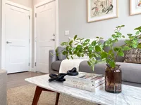 The small details matter. This space is easy to make your own. Chic and cozy living room with a plush gray sofa, stylish marble coffee table with decor and books, and vibrant green plant inviting warmth and elegance.