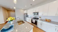 Modern, functional, and packed with storage space that actually fits real life. Modern kitchen with sleek granite countertops, stainless steel appliances, and elegant white cabinetry, accentuated by warm wood floors and vibrant floral decor.