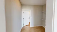A walk-in closet that connects your bedroom to your bathroom without skipping a beat. Bright walk-in closet with beige walls, carpeted flooring, and built-in shelving, leading into a well-lit room.