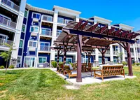 Charming apartment building with modern balconies and inviting outdoor pergola seating area, perfect for relaxing under clear blue skies.