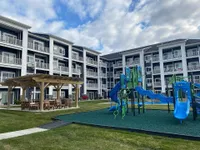 Modern apartment complex with inviting balconies, a vibrant playground, and a charming outdoor seating area under a pergola.