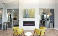 Modern apartment lounge with a sleek fireplace, bright yellow chairs, and artistic decor creating a cozy, stylish atmosphere.