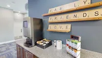 Inviting coffee station with modern decor, featuring motivational Scrabble-style wall art and a selection of Tazo teas.