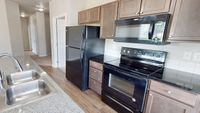 Modern kitchen featuring sleek granite countertops, dual sinks, and contemporary black appliances in a bright open space.