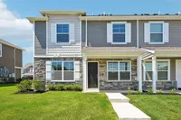 Charming modern townhouse exterior with stone accents, inviting front porch, and lush green lawn under a clear blue sky.