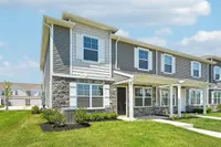 Charming two-story townhouse with modern design, stone facade, and lush green lawn under a clear blue sky.