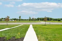 Inviting view from a fresh, green lawn overlooking a wide, open field with vibrant blue skies and fluffy clouds.