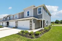 Elegant townhouse with modern siding and stone accents, featuring double garage and well-maintained front garden under a clear blue sky.