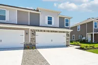 Modern townhouse exterior with a double garage, sleek siding, and stone accents, set in a sunny and vibrant neighborhood.