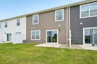 Charming townhouse with modern siding, lush green lawn, large windows, and inviting patio doors for a bright living experience.