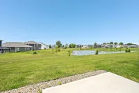 Charming neighborhood scene with lush green lawns, modern homes, and a serene pond under a clear blue sky.