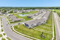 Tranquil suburban community with elegant row homes, lush green lawns, and a serene pond with a fountain, offering a picturesque neighborhood vibe.