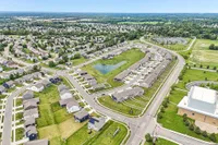 Charming suburban neighborhood aerial view showcasing well-planned streets, modern homes, and lush green spaces with a central pond.
