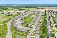 Charming aerial view of a vibrant suburban neighborhood with modern homes, lush green lawns, and a serene decorative pond, ideal for family living.