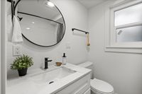 Elegant modern bathroom with a chic round mirror, sleek black fixtures, and a bright window illuminating a stylish vanity.