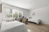 Bright and inviting bedroom with two cozy beds, a modern study desk, and large windows allowing natural light.
