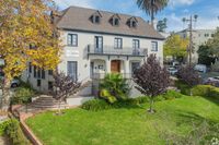 Charming three-story residential building with elegant dormer windows, lush greenery, and a welcoming staircase entrance.