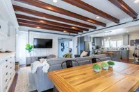 Luxurious open-concept living room and kitchen featuring modern decor, exposed wooden beams, and abundant natural light.
