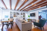 Bright and elegant living room with exposed wooden beams, cozy seating, and a stylish dining area, offering a perfect blend of modern design and comfort.