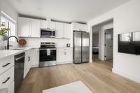 Modern kitchen with sleek white cabinets, stainless steel appliances, and elegant wood flooring, flowing into a bright, open-concept living space.