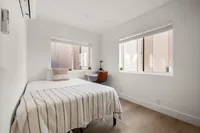 Bright and cozy bedroom featuring a comfortable bed with striped linens, large windows, and sleek wooden flooring.