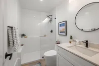 Modern bathroom with elegant white decor, featuring a spacious glass-enclosed shower, sleek vanity, and stylish black fixtures.