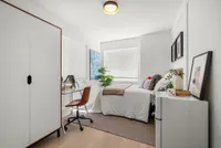 Bright and airy bedroom with modern decor, featuring a cozy bed, sleek desk area, and natural light streaming through large windows.