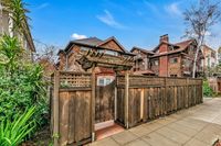 Charming wooden entrance with pergola leads to a rustic multi-story home, surrounded by lush greenery under a bright blue sky.