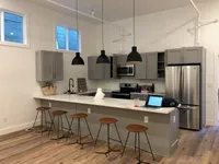 Modern kitchen space with sleek gray cabinets, stainless steel appliances, and chic pendant lighting above a spacious breakfast bar with stylish stools.
