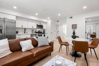 Elegant and modern open-concept living space with rich brown leather furnishings, sleek kitchen with stainless steel appliances, and cozy dining area, perfect for contemporary lifestyles