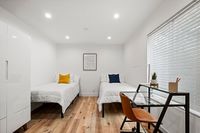 Bright and modern bedroom with twin beds, elegant wood flooring, and a stylish workspace by the window.