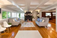 Elegant living room featuring cozy gray sofas, vibrant hardwood floors, large windows with green views, and a modern entertainment center with a fireplace.