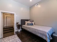 Charming bedroom with a cozy single bed, stylish pillows, and elegant wood flooring, complemented by modern lighting and a tasteful potted plant.