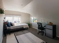Bright and cozy attic bedroom with modern decor, featuring a comfortable bed, stylish desk area, and large windows offering scenic city views.